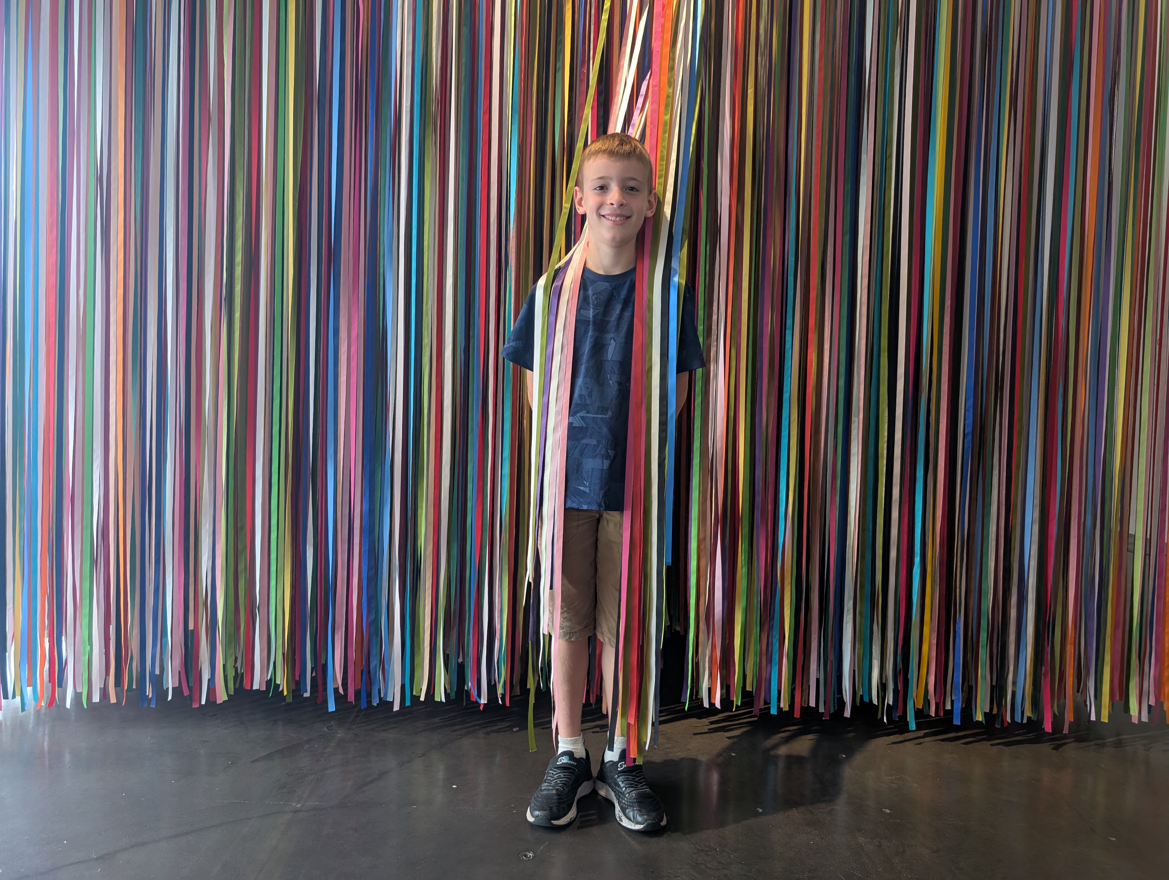 Alo Dubin, owner of Alo's Package Delivery, smiling in front of a colorful wall of streamers